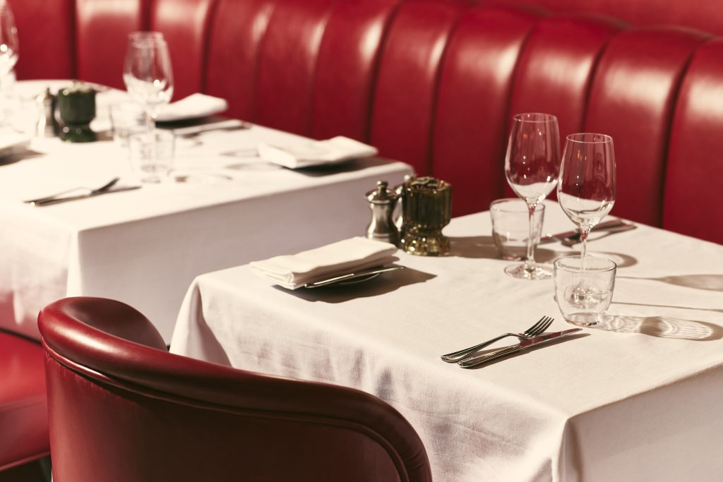 Elegant dining tables with white tablecloths and red leather seating at Bistrot at Wild Honey